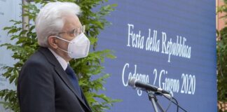 The picture shows Italian president Sergio Mattarella giving a speech in Codogno ( epicentre of the Covid-19 epidemy in Italy) on June 2nd. The president (in three-quarter profile) wears a dark blue jacket, a white shirt, a blue tie and the face mask. Behind the speaker and the microphone there are some palnts and a blue backdrop whit the white writing "Festa della Repubblica. Codogno 2 Giugno 2020" on it