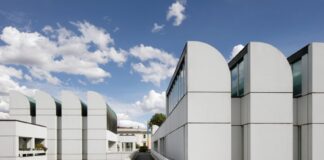 Under a blue, slightly cloudy sky, an architectural complex stands out formed by white, geometric blocks