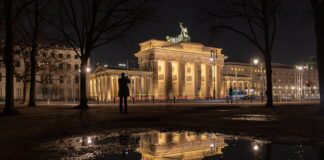 in uno spazio urbano di notte una persona fotografa un monumento illuminato e riflesso in una pozzanghera