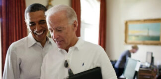 in the colored photo you can see two men, Barack Obama and Joe Biden. Biden wears glasses on the shirt and puts in his hands a tablet and a tape recorder.